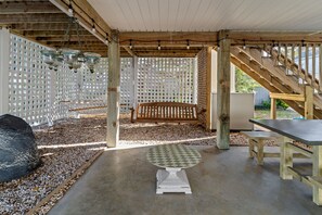 An outdoor patio area with a wooden bench, a table, and a lattice fence. - Happy Honu - Dog-Friendly Beach Retreat, Screened Porch, Walk to Beach (Kure Beach)