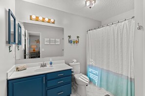 Un baño con lavamanos blanco, armarios azules, inodoro y cortina de ducha.