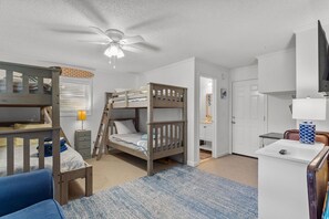 A bedroom with bunk beds, a desk, a chair, a lamp, and a ceiling fan. - Happy Honu - Dog-Friendly Beach Retreat, Screened Porch, Walk to Beach (Kure Beach)