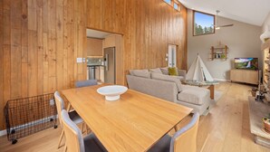A modern interior with a wooden wall, a dining area with a table and chairs, a sofa, and a television.