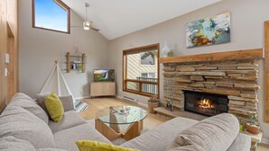 A modern living room with a stone fireplace, a large window, and a cozy sofa.
