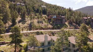 A multi-story building with a balcony on the second floor, surrounded by dense forest and a mountain in the background.