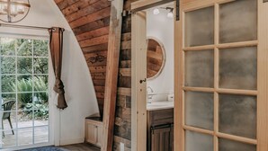 A rustic bathroom with wooden walls, a large window, and a wooden door with frosted glass panels. - 78mbr - Wood Stove - Wifi - Pets Ok - Bbq - Sleeps 6 1 Bedroom Home by RedAwning (Deming)