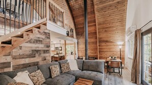 A spacious living area with a large gray sectional sofa, a wooden staircase, and a dining area with a table and chairs. - 78mbr - Wood Stove - Wifi - Pets Ok - Bbq - Sleeps 6 1 Bedroom Home by RedAwning (Deming)
