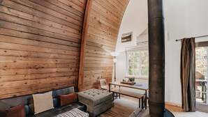 A cozy room with a wooden interior, a sofa, a bench, a table, and a large chimney. - 78mbr - Wood Stove - Wifi - Pets Ok - Bbq - Sleeps 6 1 Bedroom Home by RedAwning (Deming)