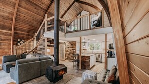 A spacious loft-style living area with a central wood-burning stove, a cozy seating area, and a kitchen in the background. - 78mbr - Wood Stove - Wifi - Pets Ok - Bbq - Sleeps 6 1 Bedroom Home by RedAwning (Deming)