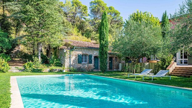 A swimming pool with clear blue water, surrounded by lush greenery and a stone building with a tiled roof. - Provencal farmhouse, warm and cozy, nestled in the heart of the pool gardens. (Salernes)