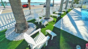 Un área junto a la piscina con sillas Adirondack blancas, una piscina pequeña y palmeras.