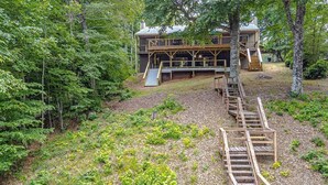 A wooden cabin with a deck and stairs leading to a second level, surrounded by dense forest. - Lake Gaston Duo Side B Kayak, Water mat, Gameroom (Bracey)