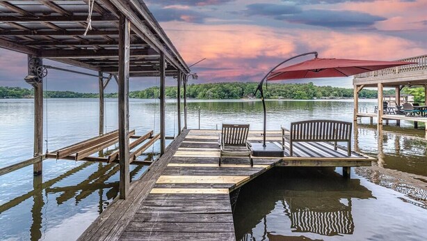 A wooden dock extending into a lake with a covered seating area and a red umbrella. - Lake Gaston Duo Side B Kayak, Water mat, Gameroom (Bracey)