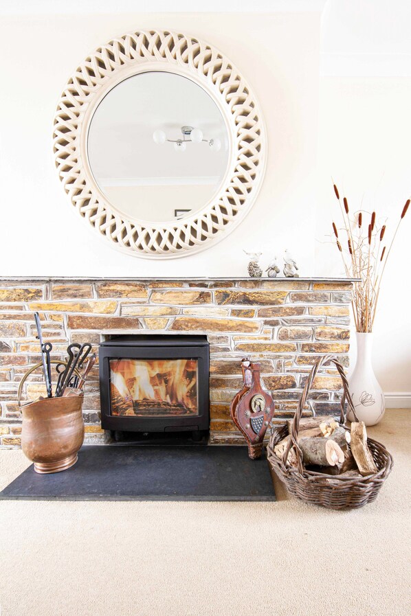 A fireplace with a stone wall, a decorative mirror, and a vase with reeds.