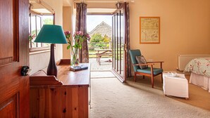 Ein gemütliches Zimmer mit Schreibtisch aus Holz, einer smaragdgrünen Lampe, einem Sessel und Blick auf einen Garten durch eine Glastür.