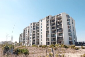 Un immeuble résidentiel à plusieurs étages, doté de balcons, situé dans une zone aride et herbeuse où la végétation est clairsemée.