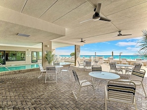 An outdoor patio with tables and chairs, a pool, and a view of the beach.