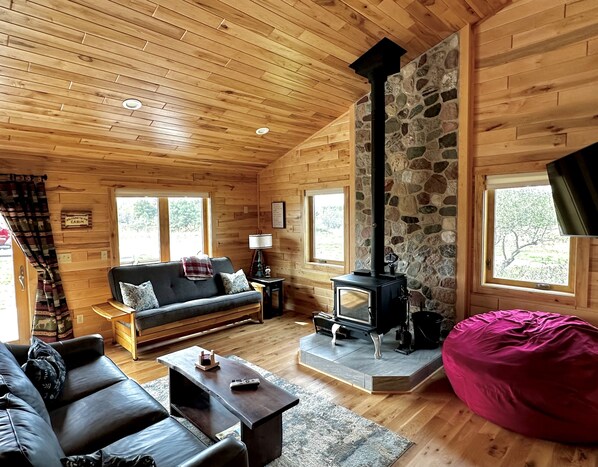 A cozy cabin interior with a stone fireplace, wooden walls, a sofa, and a bean bag.