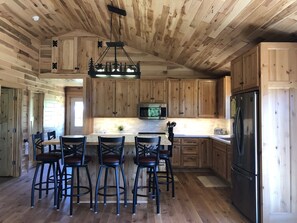 A spacious kitchen with wooden cabinetry, a central island with bar stools, a stainless steel refrigerator, and a microwave.