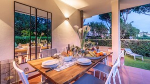 An outdoor dining area with a wooden table set for four, surrounded by white chairs. - Regina Beach, Luxury 3 bedrooms Villa by the Beach in Marina di Pietrasanta (Marina di Pietrasanta)