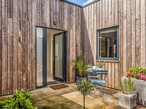 A wooden exterior with a sliding glass door, a small patio with a table and chairs, and potted plants. - Modern 2 Bedroom City Apartment With Parking - Pass the Keys (Chichester)