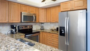 A kitchen with wooden cabinets, a stainless steel refrigerator, a microwave, a stove, and a ceiling fan. - ✨Amazing Bay Views + Amenities-Windward Point 507✨ (Fort Myers Beach)