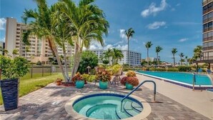 A swimming pool area with a hot tub, palm trees, and a view of a high-rise building. - ✨Amazing Bay Views + Amenities-Windward Point 507✨ (Fort Myers Beach)