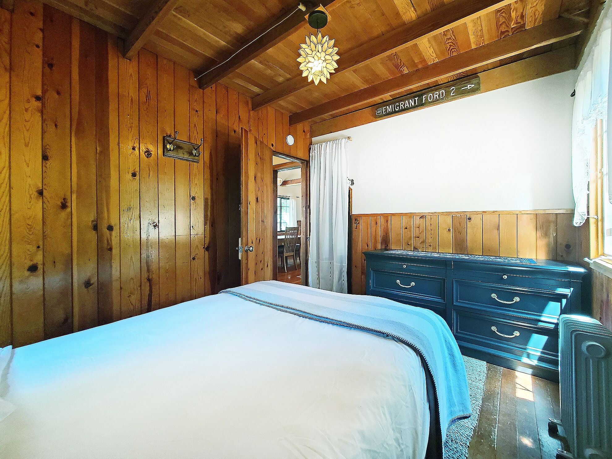 Una habitación de madera con una cama, un aparador y un cartel que dice 'EMIGRANT FORD 2'.