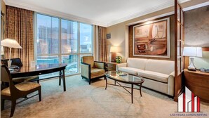 A modern hotel room with a large window, a dining area, a sofa, and a painting on the wall. - F1 Track View | Jacuzzi + Strip View Studio Suite (Las Vegas)
