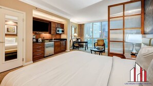 A hotel room with a large bed, a kitchenette, a dining area, and a view of the city. - F1 Track View | Jacuzzi + Strip View Studio Suite (Las Vegas)