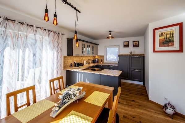 A modern kitchen with a central island, wooden dining table, and pendant lighting. - stylish holiday home, close to the cycle path and the vineyards (Naumburg)