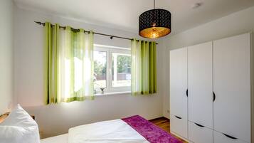 A bedroom with a bed, a wardrobe, a window with curtains, and a hanging light fixture.