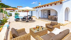 A sunlit patio with wicker furniture, a pool, and a covered outdoor dining area.