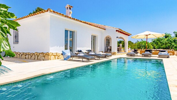 A poolside area with a white building, lounge chairs, and a clear blue pool.