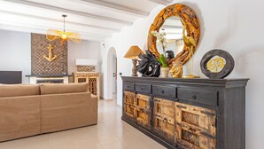 A living room with a large sofa, a dark wooden cabinet with drawers, a decorative mirror, and a wall-mounted light fixture.