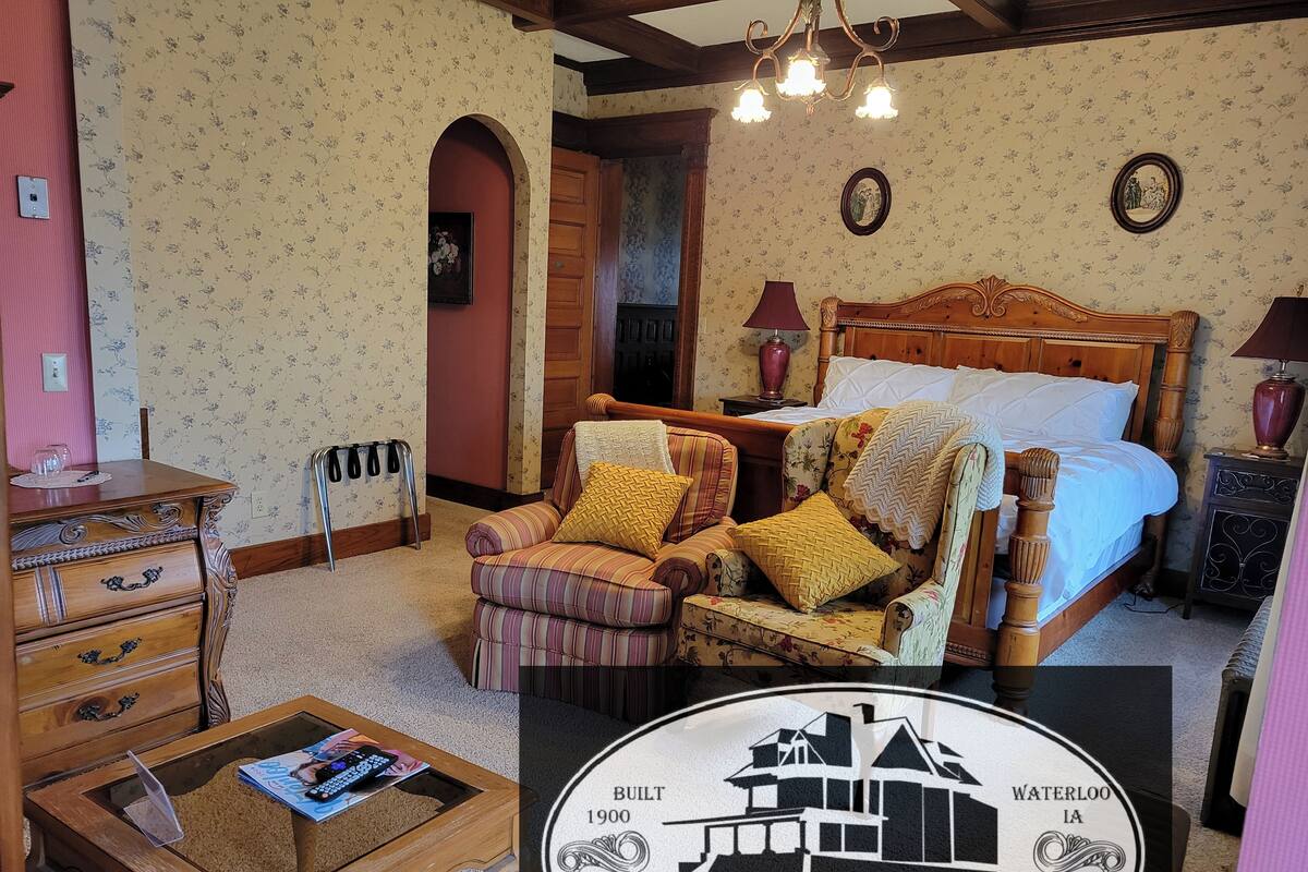 A traditional room with a large bed, a wooden chair, a small table, and a chandelier.