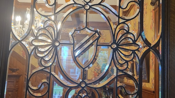 A decorative wrought iron gate with a floral pattern, leading to a room with wooden flooring and a visible bed. - The Weis Mansion (Waterloo)