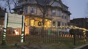 A large, historic house with a porch decorated with string lights and a sign advertising bed and breakfast services. - The Weis Mansion (Waterloo)