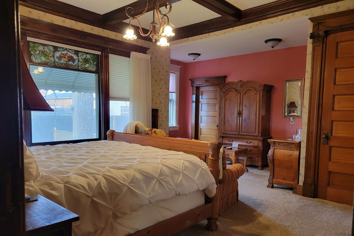 A bedroom with a large bed, wooden furniture, a window with a view, and a chandelier.