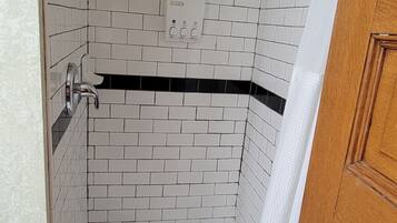 A small, enclosed shower area with white and black tiled walls, a showerhead, and a drain.