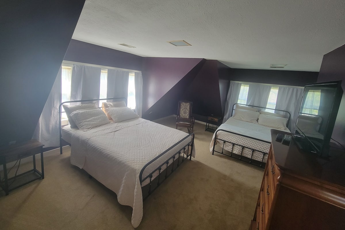 A bedroom with two beds, a chair, a desk, and a mirror.