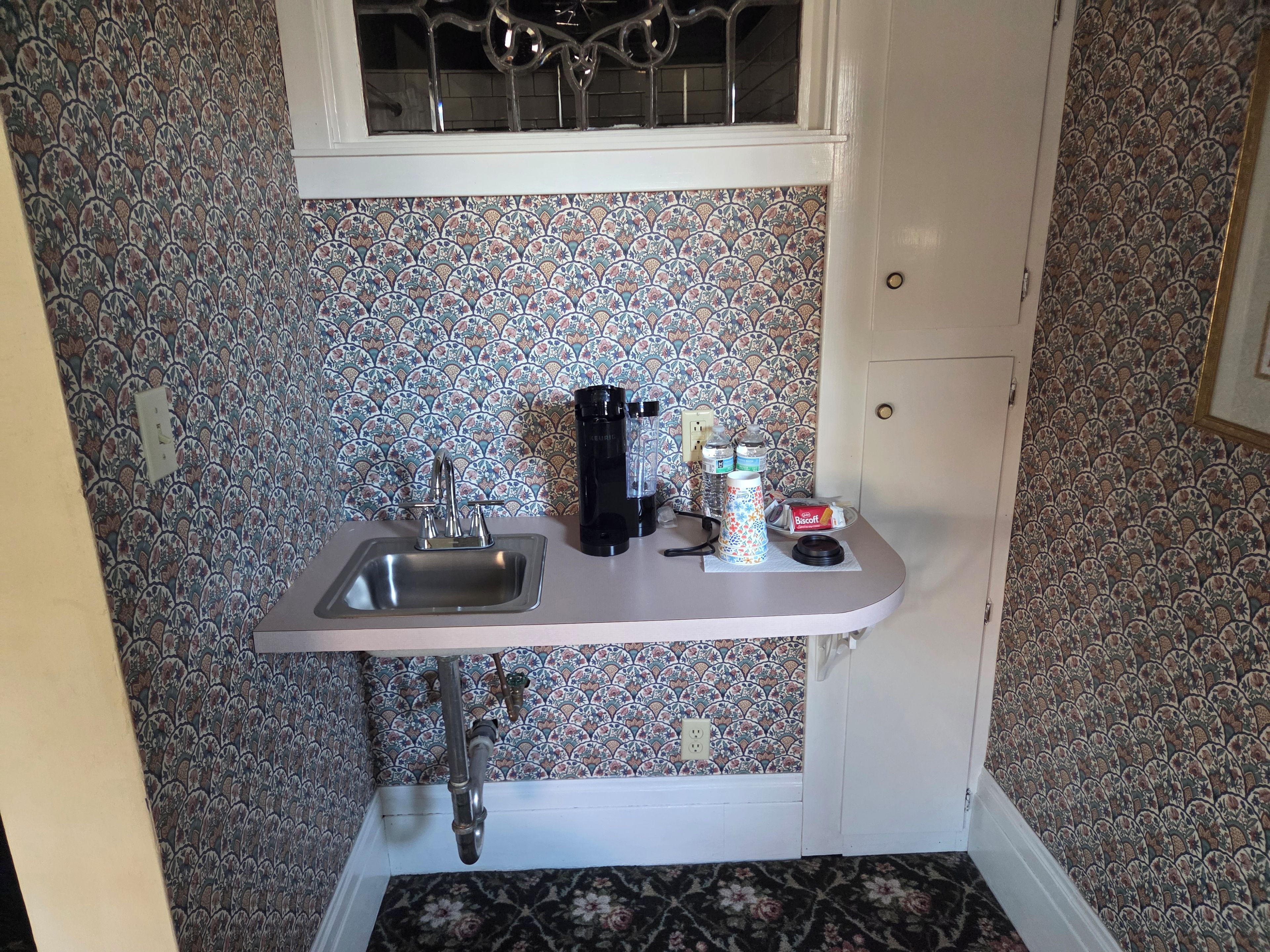 A small kitchenette with a sink, faucet, and a window above.