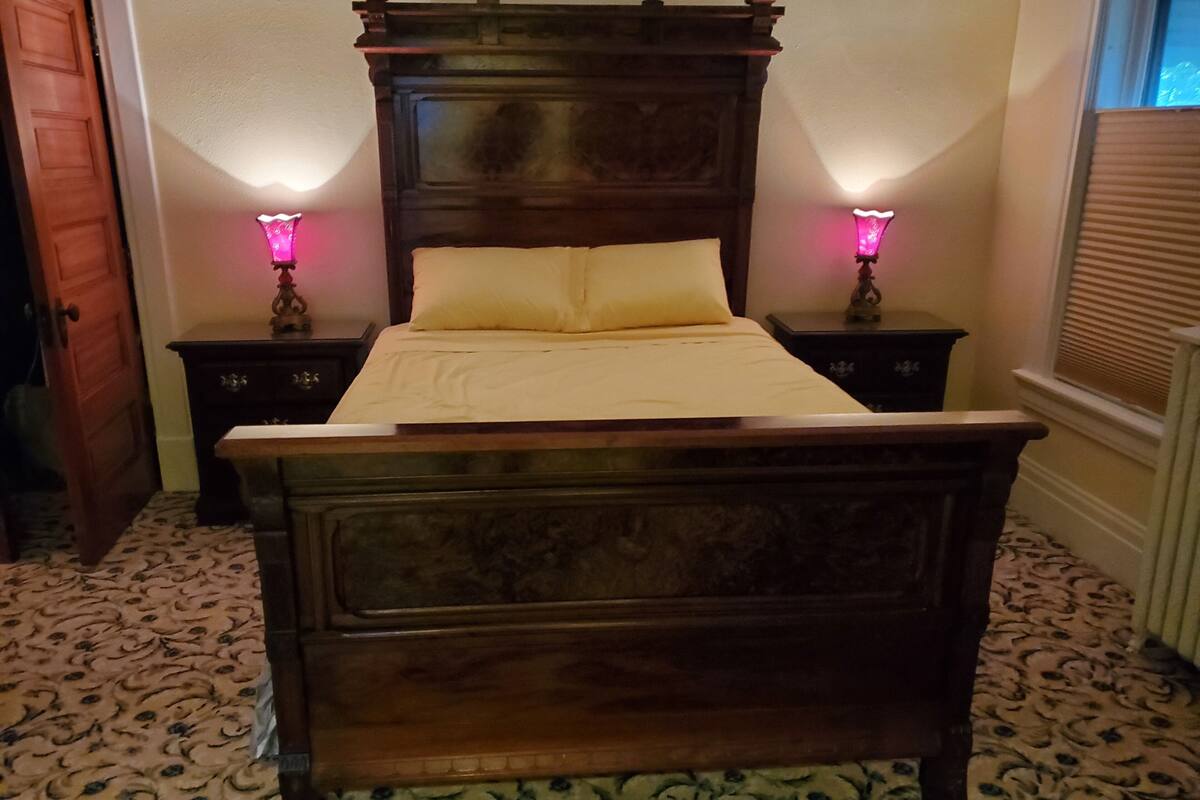 A wooden bed with a headboard, two bedside tables with lamps, and patterned carpet.