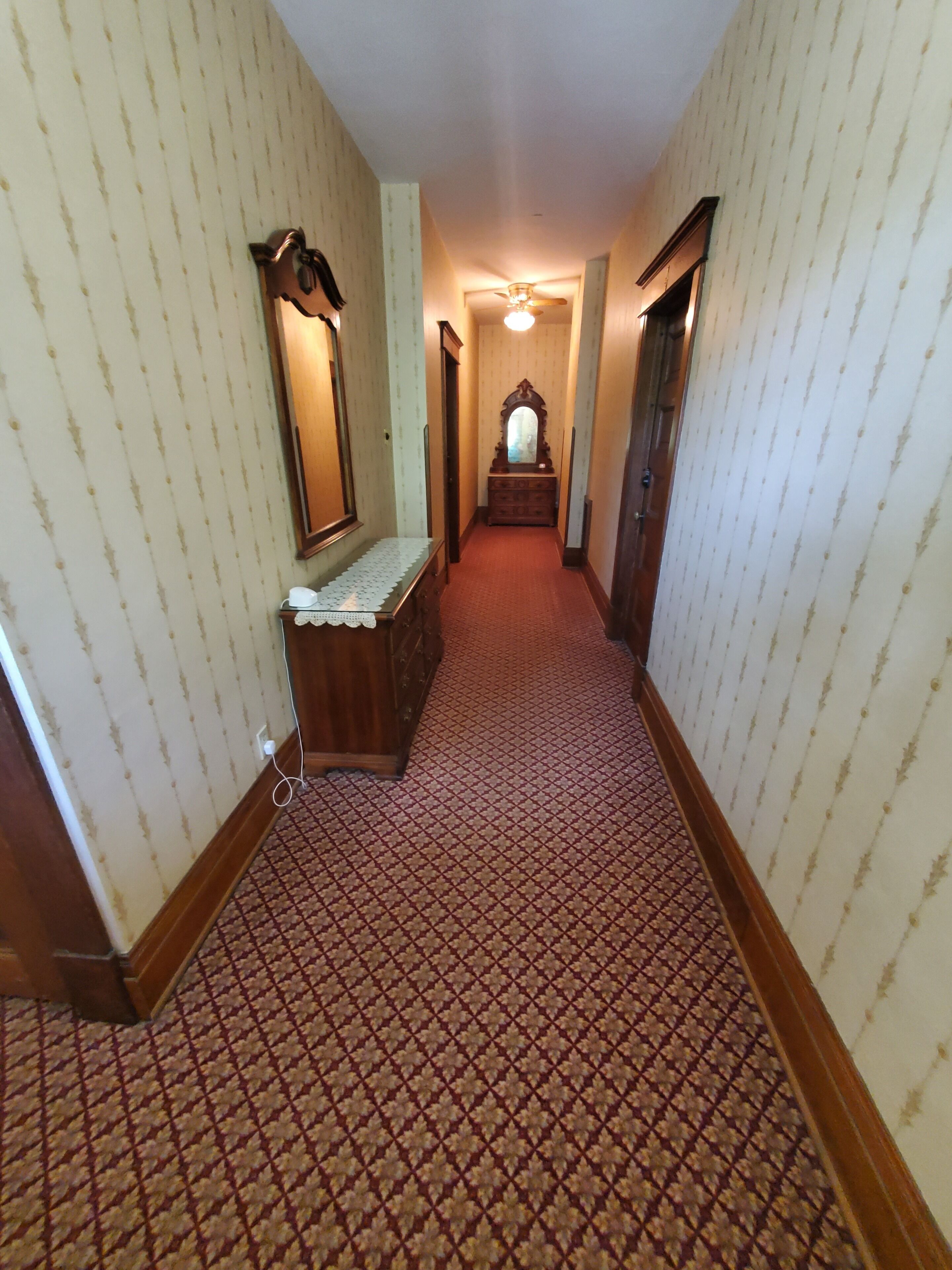 Un couloir étroit aux murs recouverts d’un papier peint à motifs, un banc en bois, un miroir et une commode.