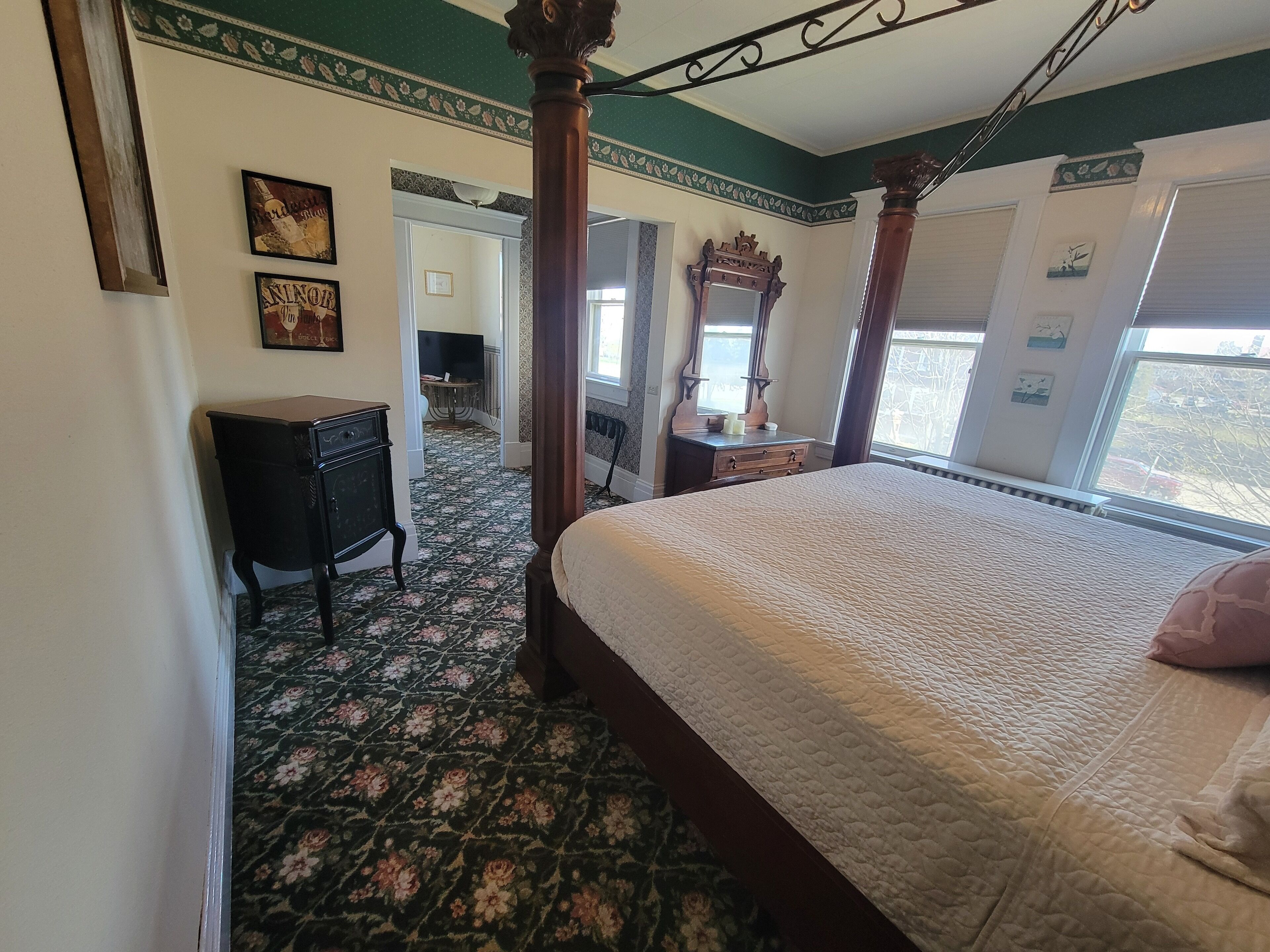 Un dormitorio con una cama con dosel, un aparador, una tocador con espejo y una puerta que da a otra habitación.