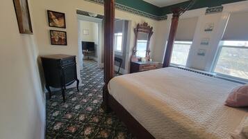 Un dormitorio con una cama con dosel, un aparador, una tocador con espejo y una puerta que da a otra habitación.