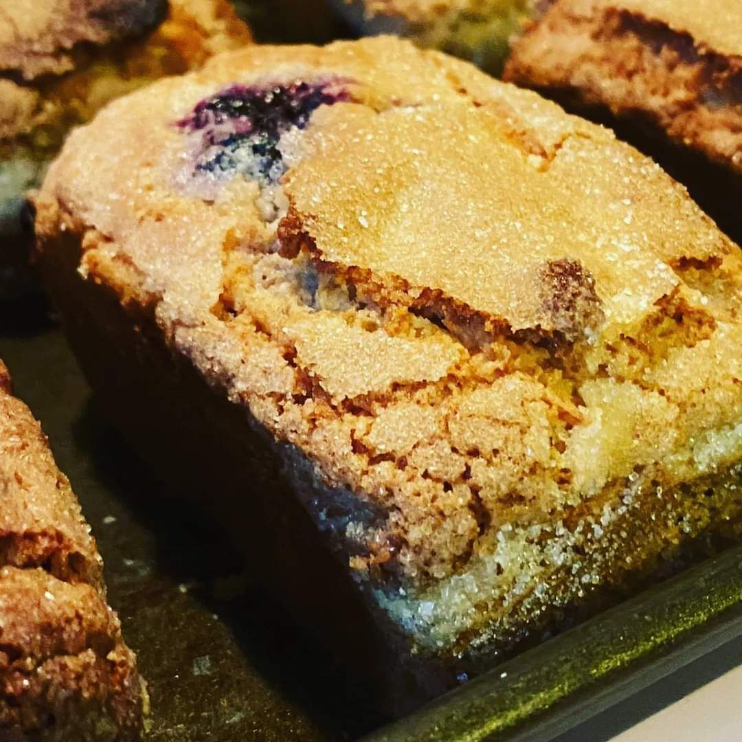 A tray of freshly baked muffins with a crumbly texture and visible fruit pieces.