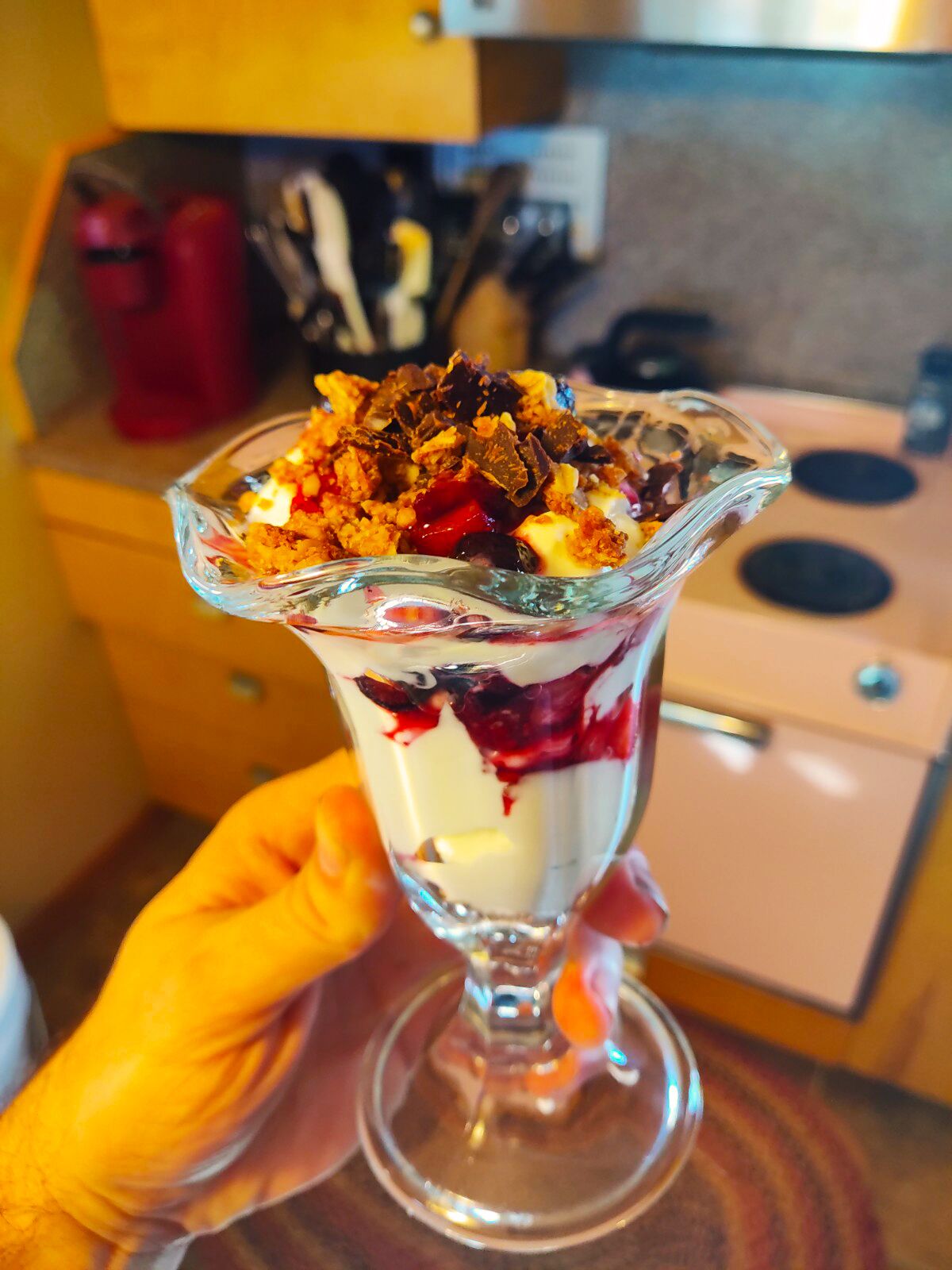 A dessert in a glass bowl with layers of cream, berries, and crumbled chocolate on top.
