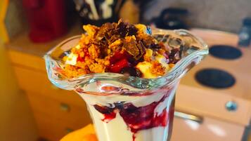 A dessert in a glass bowl with layers of cream, berries, and crumbled chocolate on top.