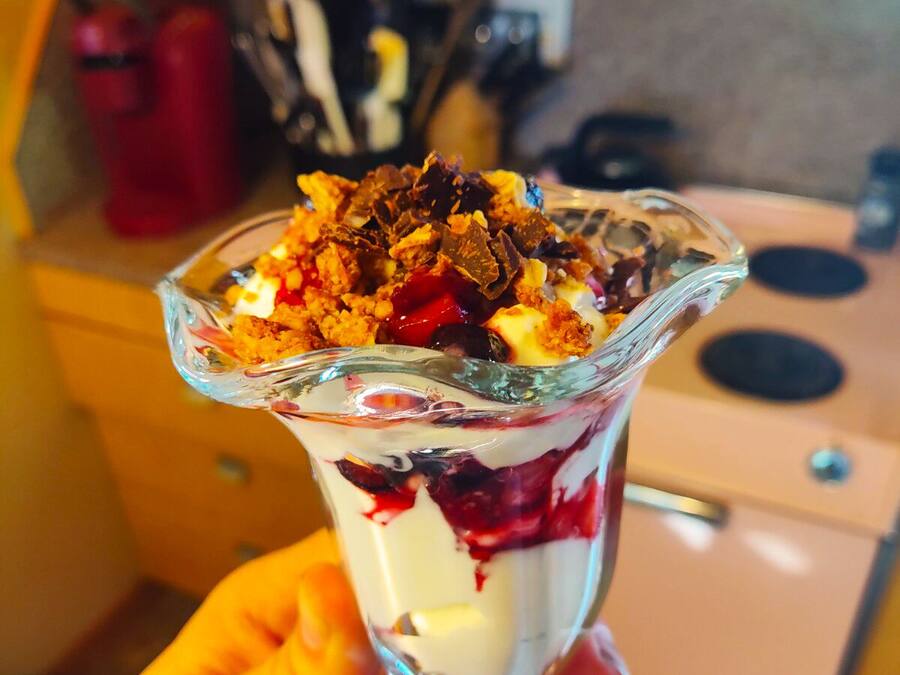 A dessert in a glass bowl with layers of cream, berries, and crumbled chocolate on top.