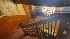 A staircase with a wooden railing, a chandelier, and patterned wallpaper. - The Weis Mansion (Waterloo)