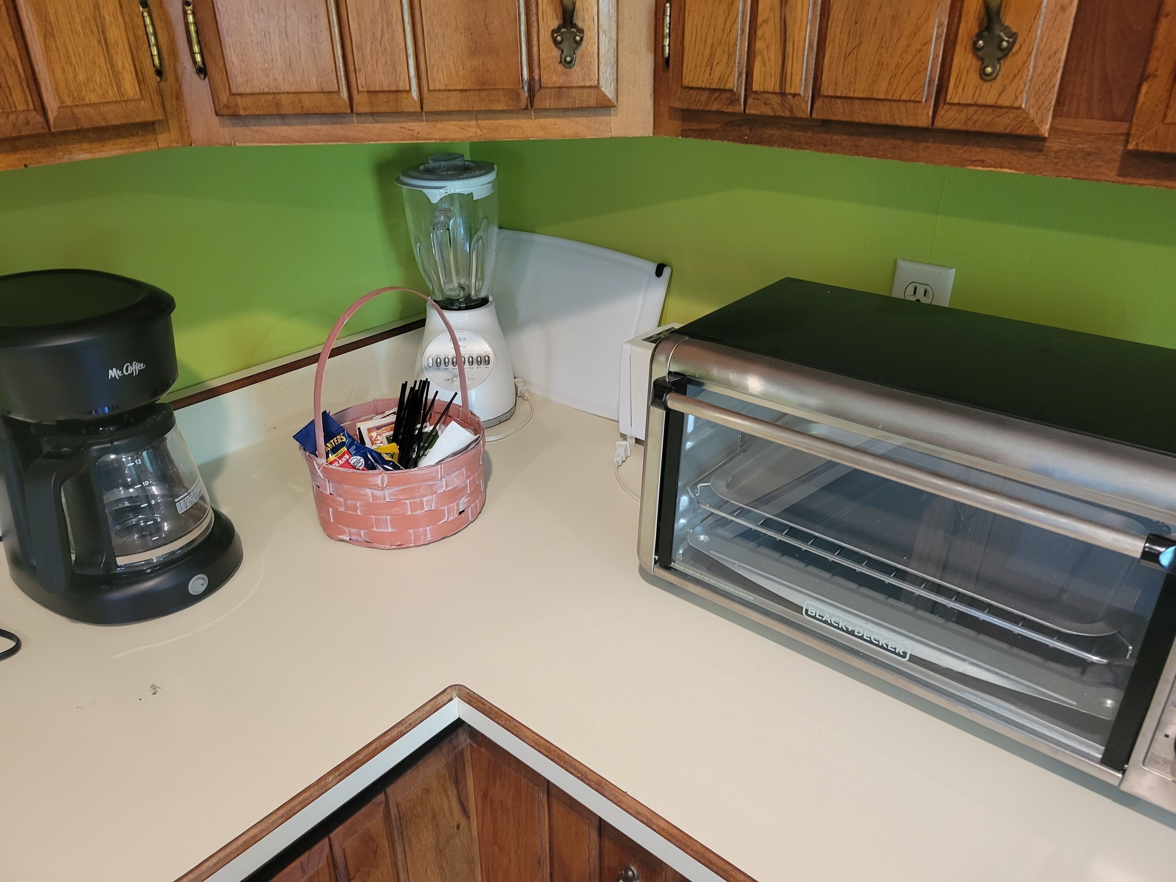 A kitchen with a coffee maker, a blender, a toaster, and a basket with utensils.