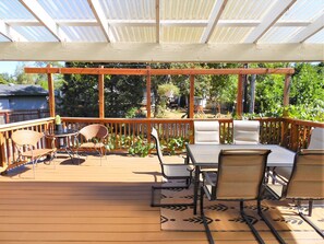 A covered outdoor deck with wooden railings, a table with chairs, and potted plants.